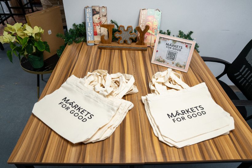 A Markets for Good tote bag hanging from a holiday-plaid vendor table